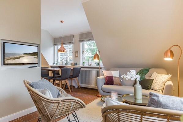 A modern living room with a sofa, chairs, a dining area, and a TV mounted on the wall.