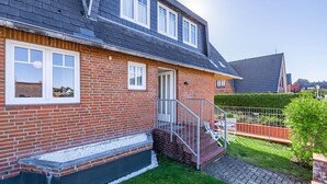 A two-story brick house with a grey roof, a front door, and a small front yard with a paved path and a metal fence. - Marienhüs - Cozy, central vacation apartment in Westerland for up to 2 (Sylt)