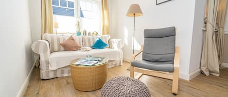 A cozy living room with a sofa, a grey armchair, a round ottoman, and a floor lamp.