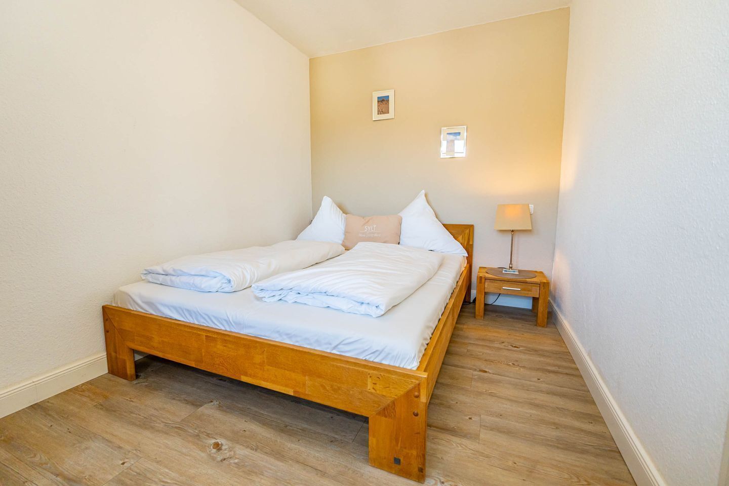 A single bed with a wooden frame, white bedding, and a nightstand with a lamp.