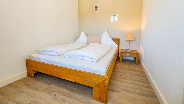 A single bed with a wooden frame, white bedding, and a nightstand with a lamp. - Marienhüs - Cozy, central vacation apartment in Westerland for up to 2 (Sylt)