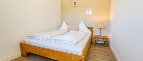 A single bed with a wooden frame, white bedding, and a nightstand with a lamp.