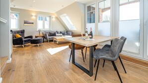 A spacious loft with a high ceiling, a dining area with a wooden table and chairs, a sofa set, and large windows providing natural light. - Sturmhaube - Apartment for max. 4 persons in Alt-Westerland with balcony. (Sylt)