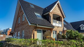 A two-story house with a steeply pitched roof, brick exterior, and a small balcony with a railing. - Sturmhaube - Apartment for max. 4 persons in Alt-Westerland with balcony. (Sylt)