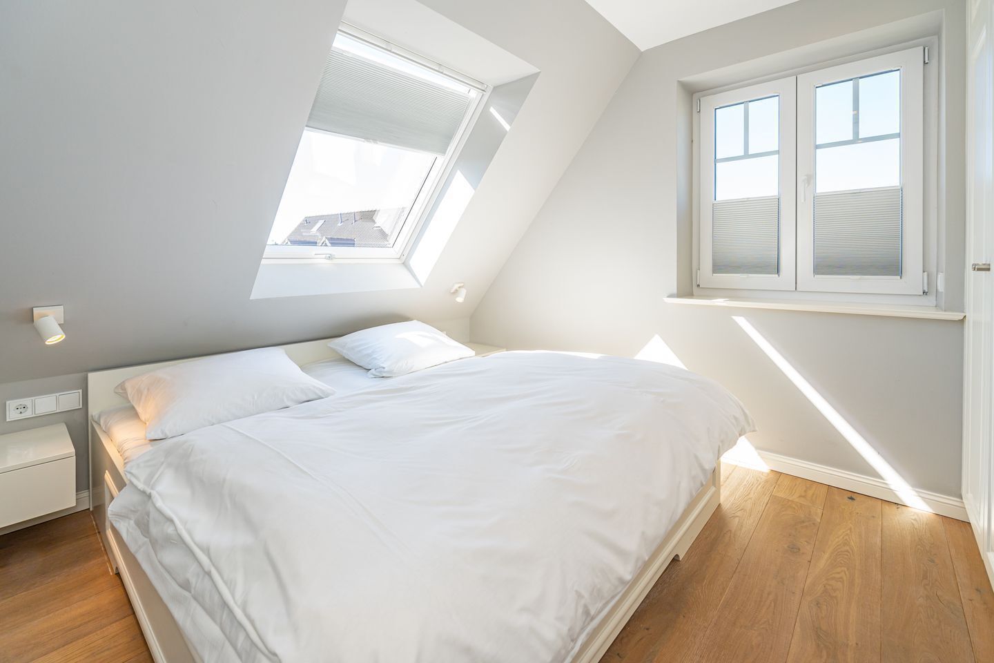 Un dormitorio con tragaluz, una cama, una mesita de noche y una ventana.