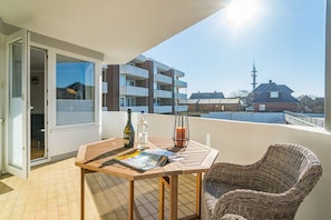 Un balcon avec une table, une chaise en osier et une bouteille de vin.