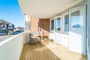 Un balcon avec un sol carrelé, une table avec des chaises et une bouteille de vin.