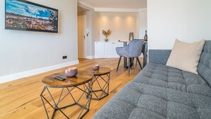 A modern living room with a grey sofa, a wooden coffee table, and a dining area with a grey chair. - Strandnest - Stylische, Neue Wohnung in Strandnähe (Sylt)