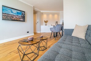A modern living room with a grey sofa, a wooden coffee table, and a dining area with a grey chair.