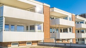 A modern multi-story residential building with balconies, brick accents, and a clear blue sky. - Strandnest - Stylische, Neue Wohnung in Strandnähe (Sylt)