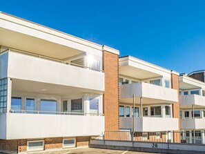 Un immeuble résidentiel moderne à plusieurs étages, doté de balcons, de détails en briques et surplombant un ciel d’un bleu éclatant.
