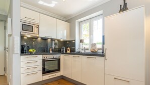 Une cuisine moderne avec des meubles blancs, un four encastré, un four à micro-ondes et une fenêtre laissant entrer la lumière naturelle.