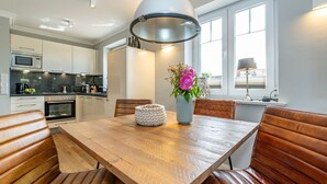 Une cuisine moderne avec des meubles blancs, une table à manger en bois et des chaises en cuir.