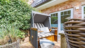 Un espace de détente extérieur accueillant, avec un fauteuil confortable et une petite table, entouré de verdure et d’un mur en briques.