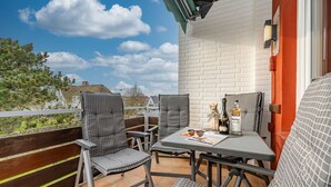 Ein Balkon mit zwei Stühlen und einem Tisch, einer Flasche Alkohol und einer Sonnenbrille auf dem Tisch.