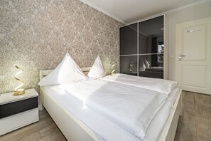 Een moderne slaapkamer met een groot bed, een nachtkastje met een lamp en een spiegel.