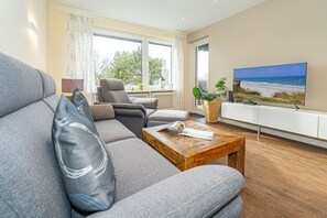 Een moderne woonkamer met een grijze bank, een houten salontafel en een televisie die een strandscène toont.