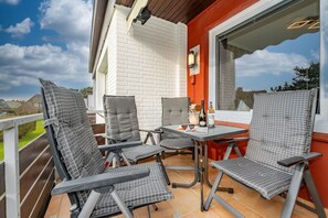 A patio with four checkered chairs and a small table, a bottle of wine, and a vase with flowers.