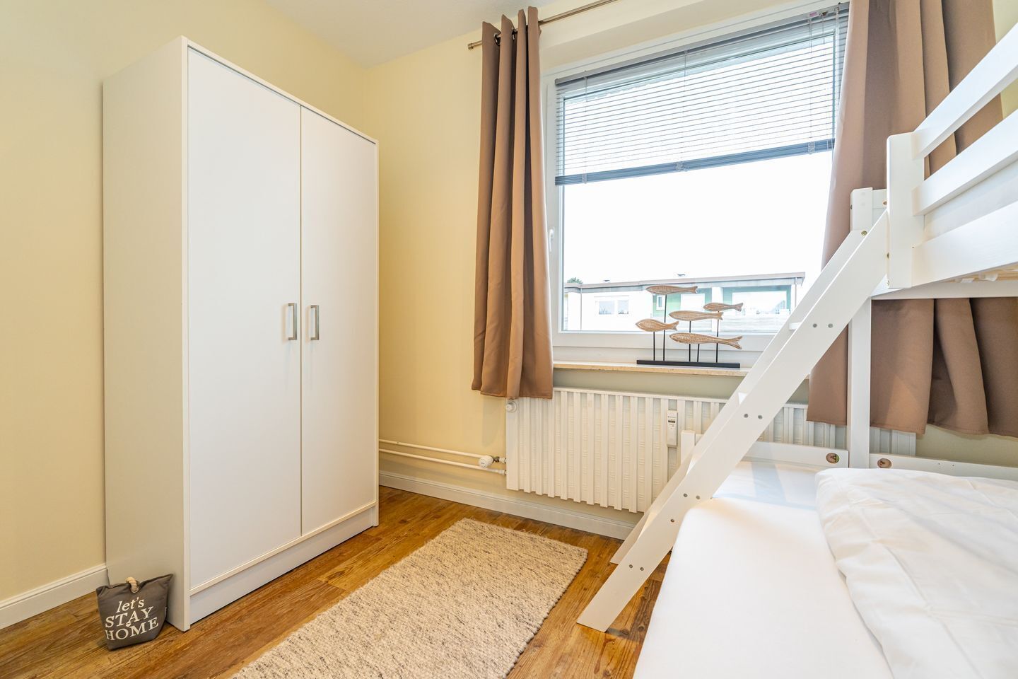 Une chambre à coucher avec un lit superposé, une armoire, une fenêtre avec des rideaux et un radiateur.