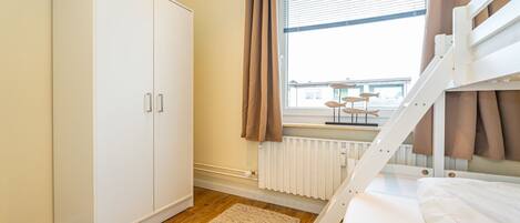 Une chambre à coucher avec un lit superposé, une armoire, une fenêtre avec des rideaux et un radiateur.