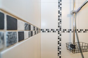 A bathroom with a tiled shower area, a shower head, and a metal shower caddy.
