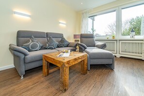 Een woonkamer met een grijze bank, een grijze fauteuil en een houten salontafel.