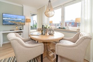 Un coin repas comprenant une table ronde, deux chaises, un lustre et une vue sur la mer grâce à de grandes fenêtres.