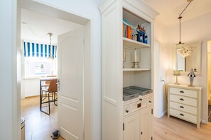 Ein Zimmer mit einem weißen Kleiderschrank, einem Schreibtisch mit Stuhl sowie einem Essbereich mit gestreifteren Vorhängen.