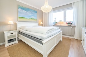 Une chambre à coucher avec un lit, des tables de chevet, un tableau, une fenêtre avec des rideaux et une vue sur l’extérieur.