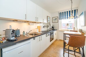 A modern kitchen with white cabinets, a Bosch dishwasher, a coffee machine, and a dining area with a striped window view.