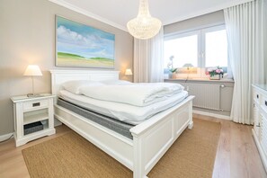 Un dormitorio con cama, mesitas de noche, un cuadro, una ventana con cortinas y vistas al exterior.