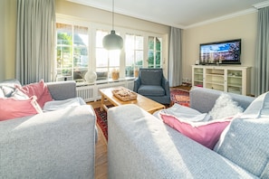 Ein Wohnzimmer mit grauen Sofas, einem Holztisch, einem grauen Sessel, einem Fernseher und einem weißen Schrank.