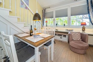 Ein gemütliches Zimmer mit einem Holztisch, einem rosafarbenen Sessel und einer Treppe mit weißen Geländern.