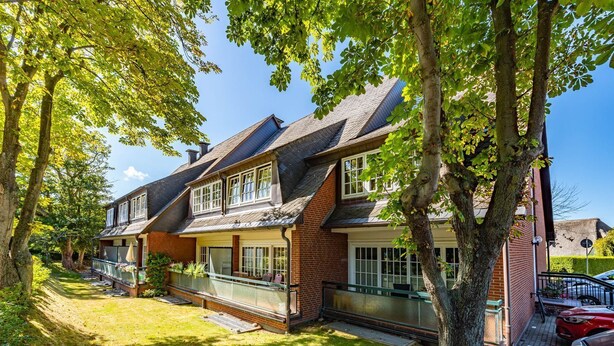 A two-story house with a balcony, brick exterior, and a well-maintained lawn.