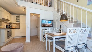 A modern kitchen with white cabinetry, a dining area with a wooden table and white chairs, and a staircase with a white railing.