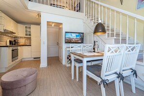 A modern kitchen with white cabinetry, a dining area with a wooden table and white chairs, and a staircase with a white railing.