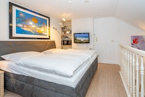 Ein Schlafzimmer mit einem Bett, einem Gemälde, einem Fernseher und einem Bücherregal.