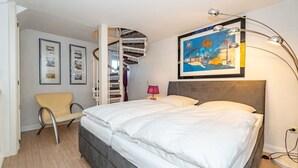 A bedroom with a large bed, a chair, a staircase, and a painting on the wall.