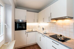 Eine moderne Küche mit weißen Schränken, einem Backofen, einer Spüle, einer Kaffeemaschine und einem Herd.