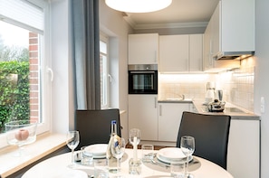 A modern kitchen with white cabinets, a built-in oven, and a dining area with a table set for four.
