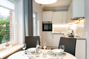 Eine moderne Küche mit weißen Schränken, einem eingebauten Backofen und einem Essbereich mit Tisch für vier Personen.
