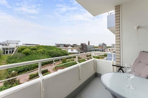 A balcony with a glass table and a wine glass, overlooking a landscaped area with buildings in the background.