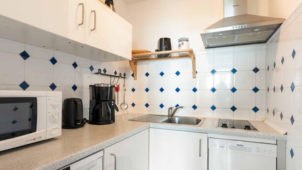 A modern kitchen with white cabinets, a microwave, a coffee maker, and a sink. - Seestern - Maritime Wohnung mit Meerblick und Balkon (Sylt)