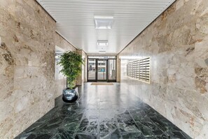 Un couloir aux murs et au sol en marbre, une plante en pot, une fente pour le courrier et une porte au fond.