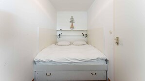 A narrow room with a bed, a small cabinet above it, and a door on the right. - Seestern - Maritime Wohnung mit Meerblick und Balkon (Sylt)