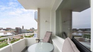 A balcony with a glass table and a wine glass, overlooking a cityscape with buildings and a park. - Seestern - Maritime Wohnung mit Meerblick und Balkon (Sylt)