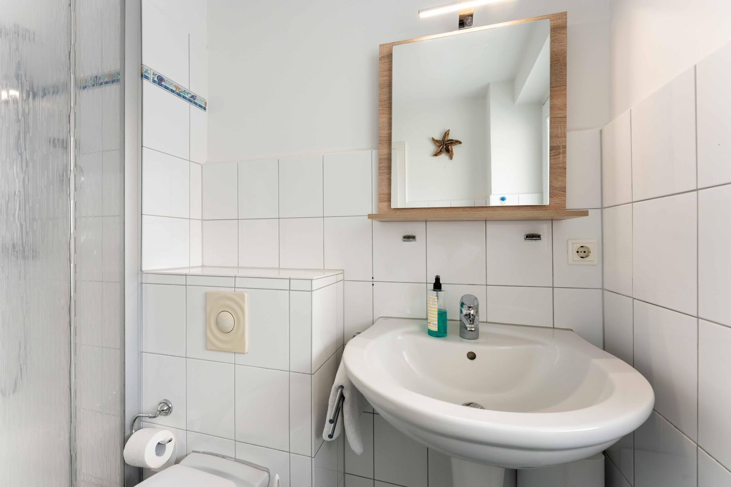 A bathroom with a white sink, a mirror, a towel rack, a toilet, and a shower area.