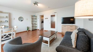 A living room with a sofa, a coffee table, a TV, and a dining area with chairs and a table. - Seestern - Maritime Wohnung mit Meerblick und Balkon (Sylt)