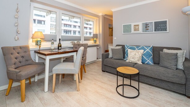 Una sala de estar moderna con un sofá gris, una mesa de comedor con sillas y una mesita redonda.