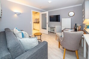 Un salon moderne avec un canapé gris, une petite table ronde et un téléviseur fixé au mur.